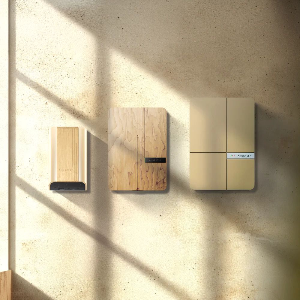 Side-by-side display of Andersen Quartz, A2, and A3 EV chargers in light wood and neutral tones, mounted on a textured plaster wall with soft natural lighting.